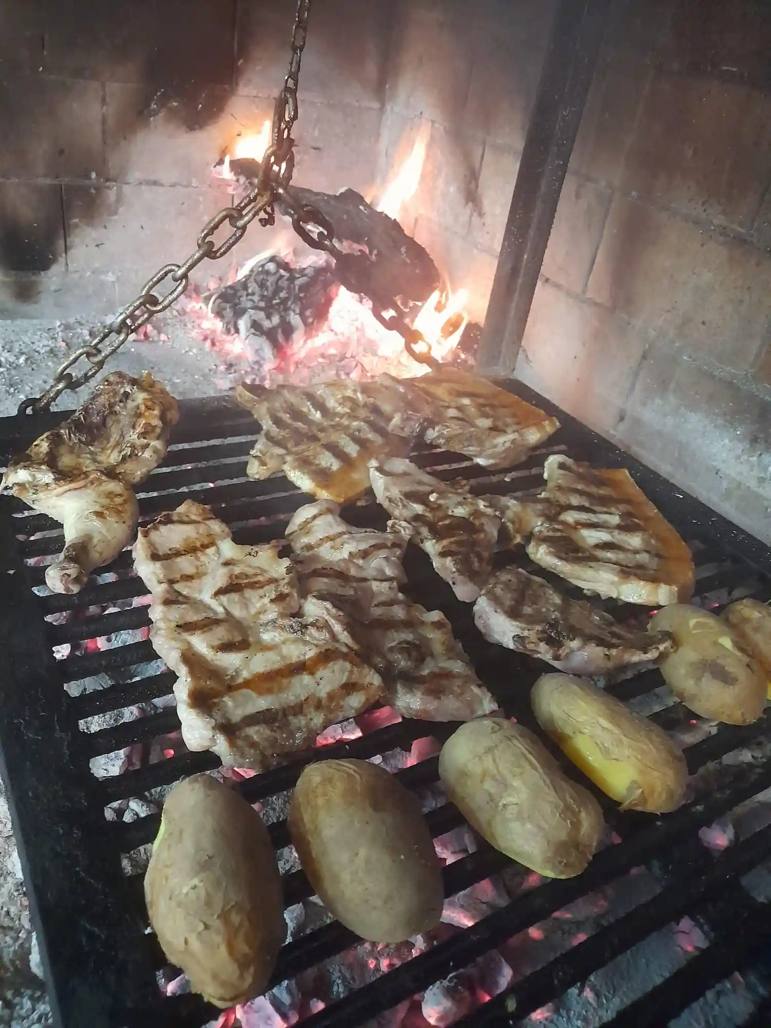 Carne y patatas asándose en la parrilla del Asador Los Toneles.